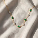 Colar dourado elegante com uma esmeralda quadrada e detalhes de cristais brilhantes