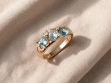 Anel dourado elegante adornado com zircónias azuis brilhantes